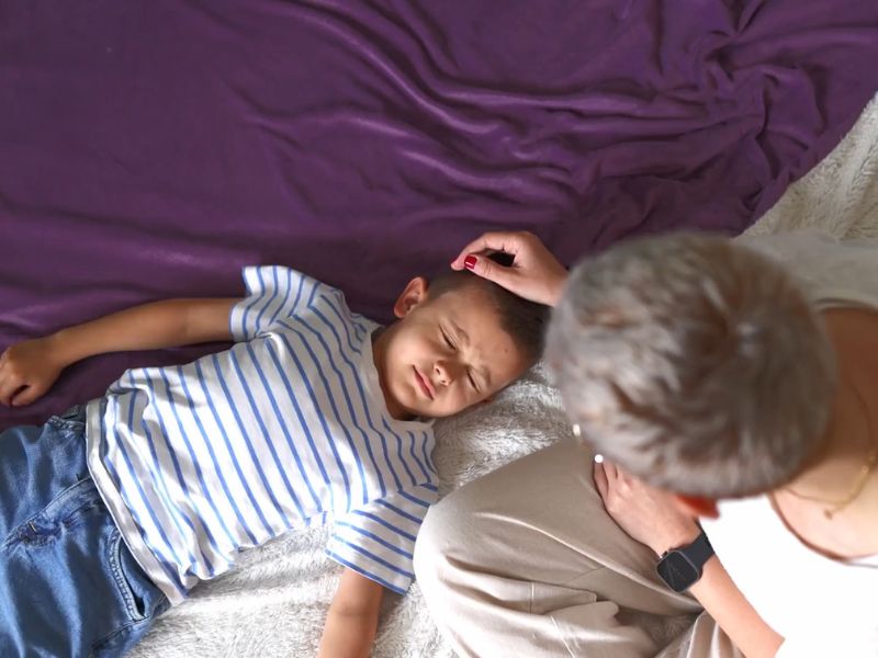 mama mazi dečaka koji leži na krevetu i boli ga glava