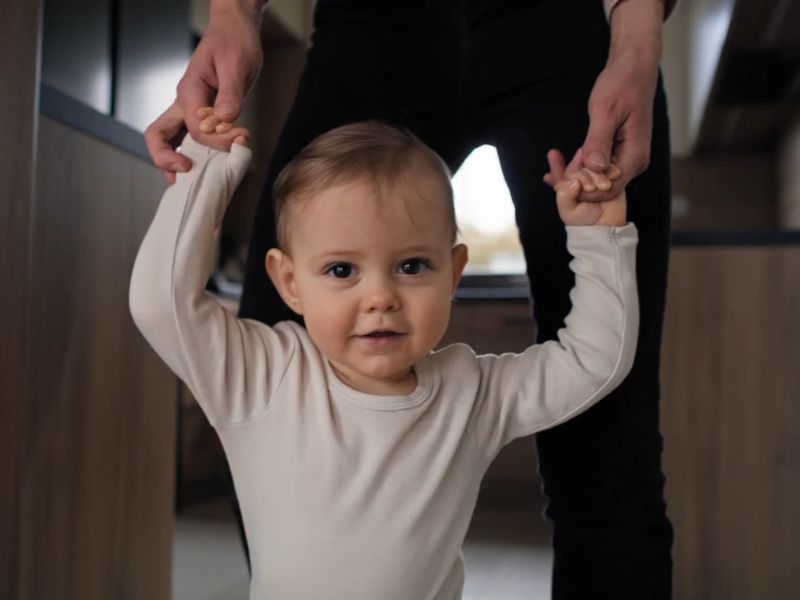 osoba drži bebu za ruke i uči je da stoji na nogama