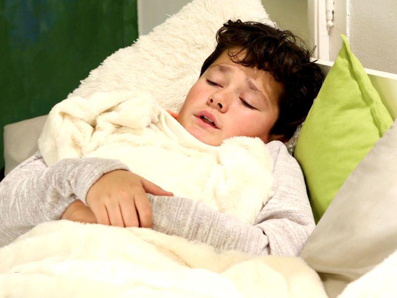 bolestan dečak leži pokriven jorganom u krevetu