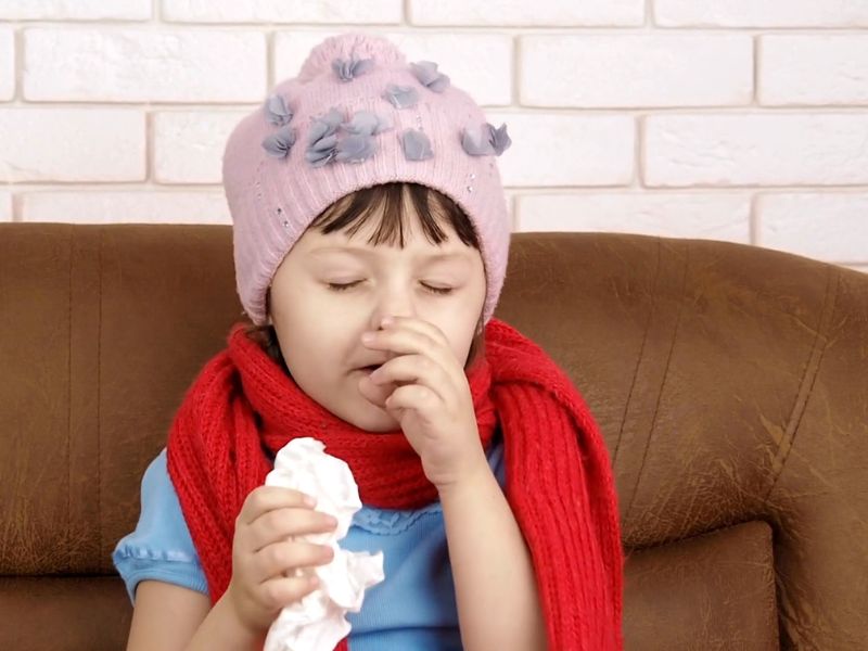 devojčica sa kapom i palom drži maramicu u ruci i kašlje