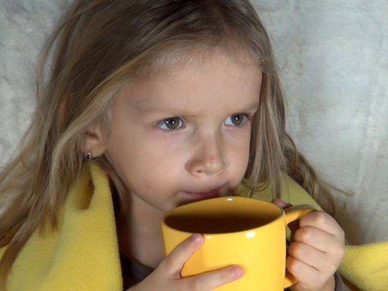 devojčica pokrivena žutim ćebetom pije čaj iz šolje